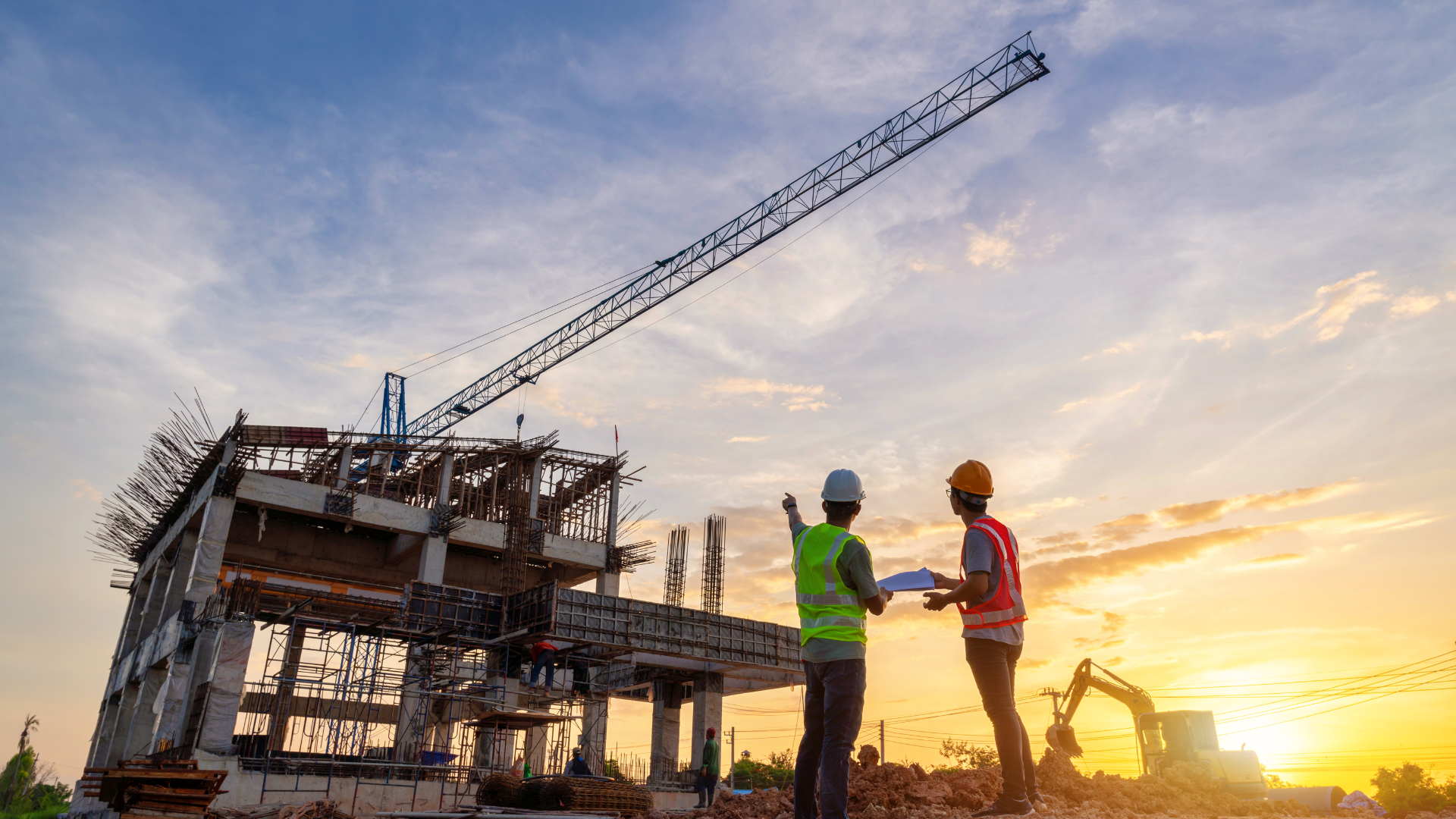Homens com capacetes e coletes de segurança, um apontando para uma construção incompleta com guindaste, ao pôr do sol.